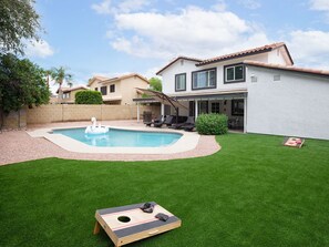 Spacious backyard with a private pool, sun loungers, BBQ, covered patio, outdoor dining, seating area, and corn hole!