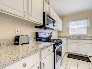 - Cook with ease in this modern kitchen featuring granite countertops and stainless appliances
- White cabinetry, gas stove, and microwave offer function and charm
- Natural light flows in through the window for a cheerful culinary space
