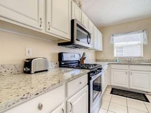 - Cook with ease in this modern kitchen featuring granite countertops and stainless appliances
- White cabinetry, gas stove, and microwave offer function and charm
- Natural light flows in through the window for a cheerful culinary space