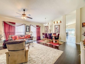 - Cozy living room with plush seating, rich drapes, and warm decorative touches
- Dining table set for six, framed by elegant wall art and pendant lighting
- Open layout connects seamlessly to the kitchen and pool area beyond