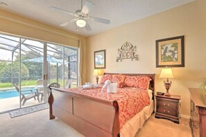 The main floor master bedroom offers a king-size bed, ceiling fan, smart TV, sliding doors to the pool area, a full dresser, a walk-in closet, and an ensuite