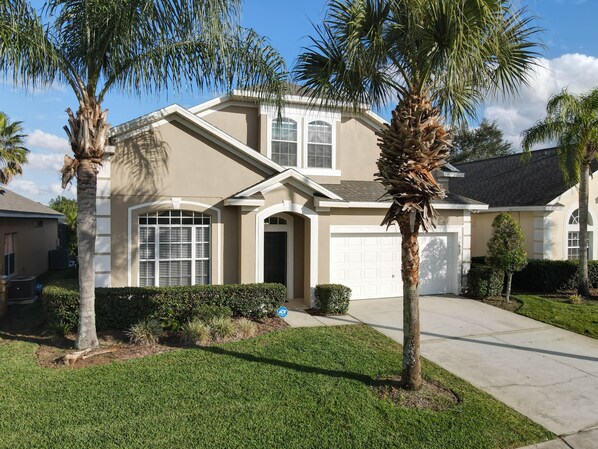 Elegant two story villa framed by tall palm trees, boasting crisp landscaping, large shuttered windows, and a bright white garage door.