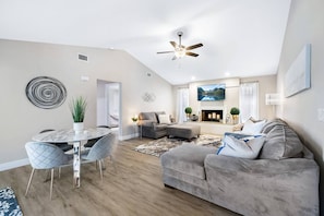 Spacious, open-concept living room featuring a cozy oversized bean bag, extra seating/game table, and a large smart TV for entertainment. Perfect for relaxing and gathering with your group!
