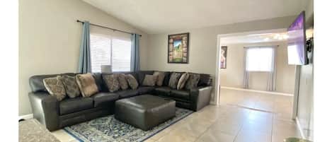 Large living room with leather sectional sofa, ottoman, and Smart TV