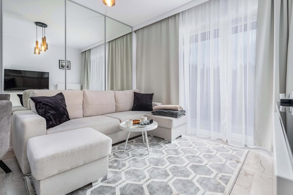 A bright, cosy living room with a sofa bed. The space is enlarged by a mirror located behind the sofa. Stylishly chosen accessories and soft textiles add to the cosiness of the interior. 
