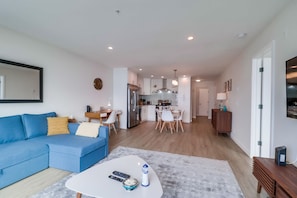 View of living space with pull out queen sofa bed, work space with desk and open-style kitchen with dining for 5 guests. The back foyer leads to the guest bedroom and separate bathroom