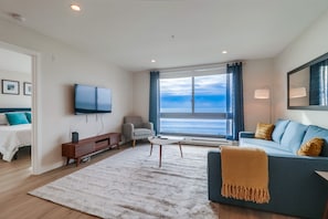 Living room with ocean view, adjustable blinds and curtains, smart TV and pull out queen sofa bed. Peek into master bedroom