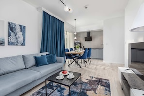 Living and dining area with a blue sofa, a small dining table, and blue curtains, creating a cozy and unified look.