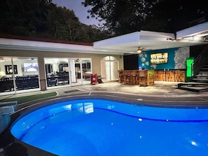 Luxury pool deck with covered bar and HDTV. Poolside drinks and relaxation.