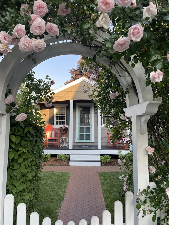 A view through a rose covered trellis at a quaint vacation cottage in Provincetown with a front porch with rocking chairs
