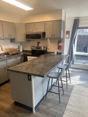 Full, well- lit full kitchen with bar stool seating.