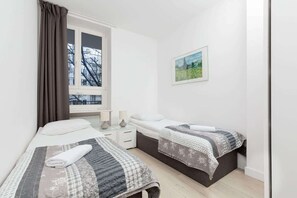 A cosy bright bedroom with two single beds on which lies a grey bedspread.