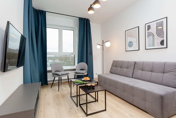 A comfortable living room featuring a stylish gray sofa, a sleek flat-screen TV on a wooden stand, and a minimalist coffee table. Perfect for unwinding in a calm and neutral space.
