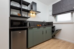 A stunning kitchen design featuring deep green cabinets with brass handles, a pristine white tiled backsplash, and open shelving for an organized and stylish look. Ideal for cooking enthusiasts seeking both functionality and aesthetics.