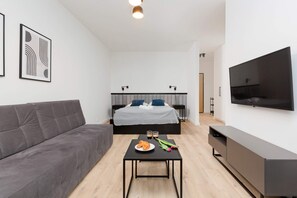 A contemporary and inviting living room featuring a gray sofa, accented by a large flat-screen TV and natural wooden floors. Perfect for relaxing or entertaining guests in a bright and vibrant setting.