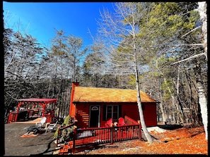 Front of cabin features patio with Adirondack chair, Fire Pit & Pergola w/ BBQ