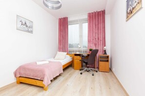 A minimalist bedroom with a single bed, study desk, and pink curtains, perfect for a peaceful and functional living space.