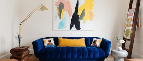 Cozy living room with a large blue velvet couch. Bright and fun. Perfect for lounging or hosting.