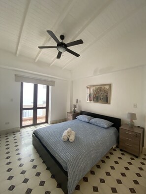 Spacious bedroom with queen-sized bed, fan, AC and little balcony.