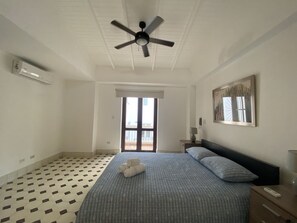 Spacious bedroom with queen-sized bed, fan, AC and little balcony.