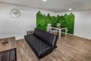 A modern and inviting space featuring a sleek black futon, a stylish coffee table, and a charming dining nook with a green mountain mural accent.