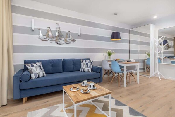 A cozy living room featuring a stylish blue sofa, a glass coffee table, and warm wooden flooring. The decor is modern, with subtle accents and soft lighting.