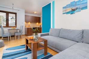 A view of the living and dining spaces combined, showcasing a gray couch, a wooden coffee table, and a dining set for four with a vase of flowers on the table.
