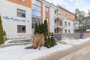 A view of the building named "Villa 4 pory roku" with a snowy landscape and a modern facade. The building has large windows and appears surrounded by trees.