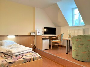 Einzelbett mit Blick zum Schreibtisch und kleinem Kühlschrank