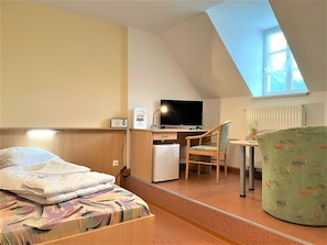 Einzelbett mit Blick zum Schreibtisch und kleinem Kühlschrank
