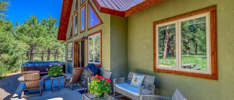 The back patio is a slice of heaven with a bubbling hot tub, grill, outdoor seating, and swaying pine trees.