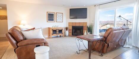 Bright & open living room with recliner couches, smart TV, and back patio sliding glass doors.