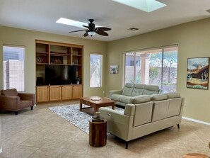 Bright, spacious living room with 65" TV and reclining sofas.