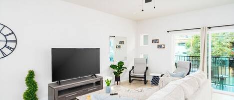 The living room boasts a stylish and clean design, offering comfort with its 65" Smart TV featuring complimentary Netflix, a sofa bed, a spacious balcony, and a variety of games for entertainment.
