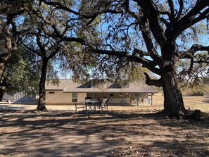 House is nestled in valley behind live oak trees