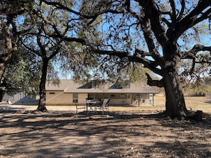 House is nestled in valley behind live oak trees