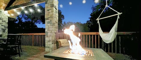 Firepit on deck at night with decorative lights on. Lots of seating & hammocks