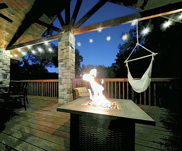 Firepit on deck at night with decorative lights on.  Lots of seating & hammocks