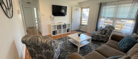 Front door opens up to living room that includes a smart tv, two chairs, couch