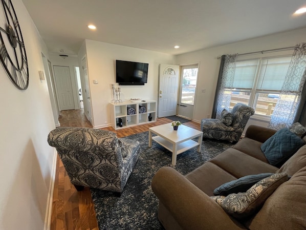 Front door opens up to living room that includes a smart tv, two chairs, couch