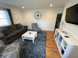 Front door opens up to living room that includes a smart tv, two chairs, couch