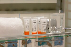 A close-up of a bathroom shelf displaying neatly arranged toiletries and rolled white towels for guests.