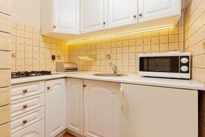A compact kitchen with white cabinets, a tiled backsplash, a microwave, and bright under-cabinet lighting creating a welcoming atmosphere.
