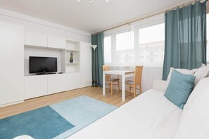 A different angle of the living room showcasing the sofa, a flat-screen TV mounted on the wall, and a blue rug adding warmth to the wooden floor.