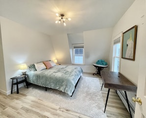 Bedroom with blackout window shades, king sized bed, mirror and desk. 