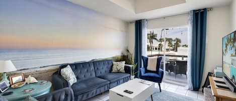 Beachy Speakeasy living room has blue velvet chairs and futon with wall mural