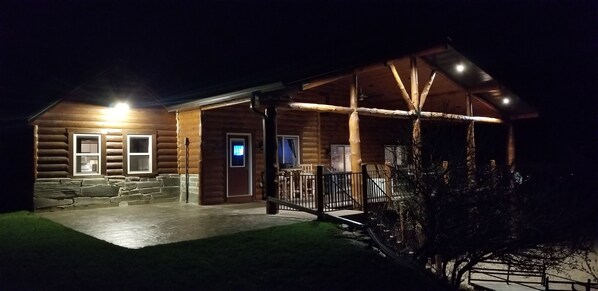 Cabin at night showing covered deck and patio.