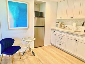 Kitchenette with a Toaster oven, microwave, fridge, Keurig coffee maker, glasses, plates, and cutlery.