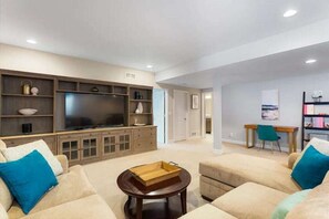 Basement Rec Room with voersized couch and smart tv for movie night along with game table and standard sized shuffle board table for entertaining and gathering.