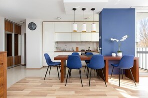 A combined dining and living area with a wooden dining table surrounded by blue chairs. The open layout creates a spacious and functional atmosphere.